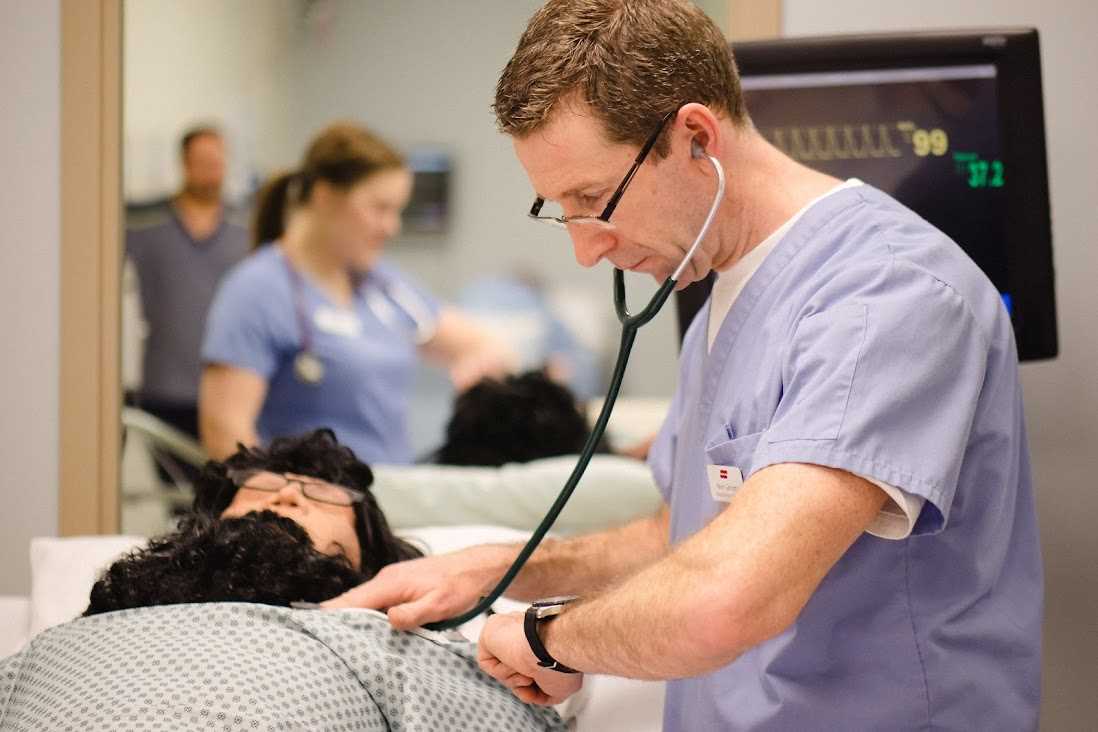 A nursing student holds a stethoscope to a mannikin patient in the health care simulation lab